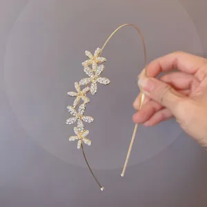 Detail view of a delicate gold thin metal headband featuring sparkling rhinestone and pearl flowers.