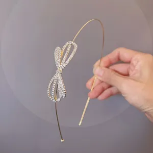 Exquisite detail view of a thin gold metal headband featuring a sparkling rhinestone bow accent.