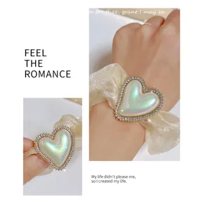 Vue détaillée de l'élastique à cheveux cœur en strass, organza scintillant et charm irisé.