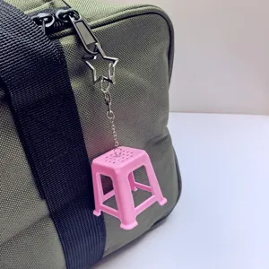Close-up detail of a cute pink mini plastic stool keychain hanging on a green canvas bag.