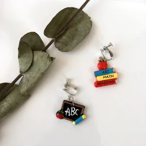 Detailaufnahme asymmetrischer Ohrringe mit Schulmotiven wie Büchern und Tafel.
