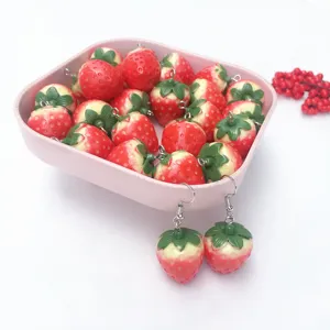Close-up detail of cute handmade resin strawberry earrings and charms set in pink tray.