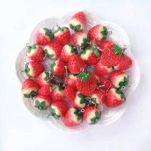 Detailed shot of cute resin strawberry earrings and clip-ons arranged on a white ceramic plate.