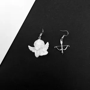 Primer plano de pendientes asimétricos barrocos vintage de ángel cupido y arco, retro.