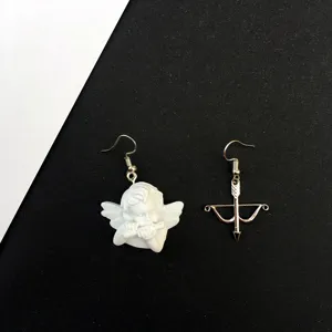 Primer plano detalle de pendientes asimétricos de ángel y arco flecha, diseño retro.