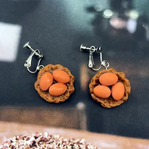 Gros plan de boucles d'oreilles fantaisie artisanales avec nid miniature et œufs en résine.