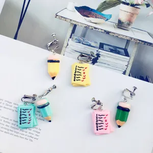 Detailed shot of creative handmade pencil and notebook asymmetric earrings, cute student style.