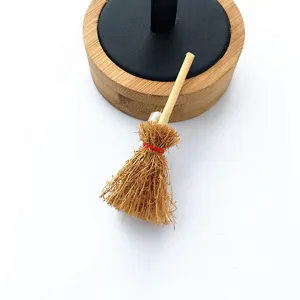 Detalle del accesorio escoba de bruja en miniatura con fibra vegetal y lazo rojo.