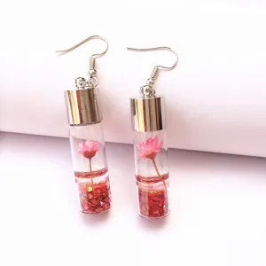 Detail shot of clear glass vial earrings featuring pink dried flowers and red glitter inside.