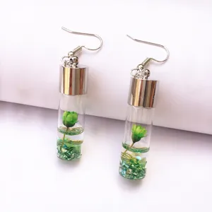 Detailed shot of handmade glass bottle earrings featuring green preserved flower and glitter.