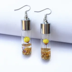 Close-up detail of glass wishing bottle earrings with yellow dried flower and gold glitter.