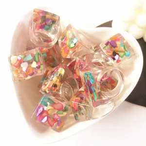 Anillos gruesos de resina acrílica transparente con piedras de colores, vista detallada.