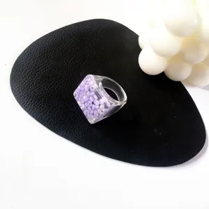 Anillo grueso de resina acrílica con cuentas moradas incrustadas, estilo minimalista, detalle.