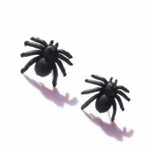Black spider stud earrings, Halloween party prank accessory, detailed close-up shot.