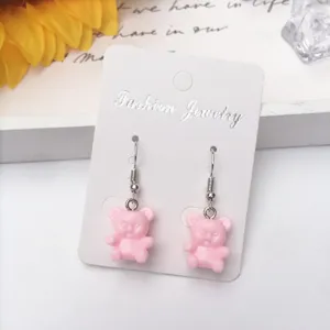 Detaillierte Nahaufnahme von süßen rosa Harz Bär Ohrringen mit Silberhaken auf weißer Karte.