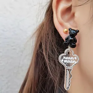 Close-up detail of cute black bear and transparent key pendant earrings, stylish fashion accessory.