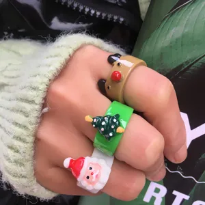 Dettaglio del set di anelli natalizi in resina colorata indossati sulle dita della mano.