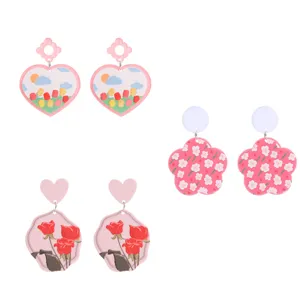 Boucles d'oreilles en acrylique rose avec motifs floraux et cœurs, vue de détail.