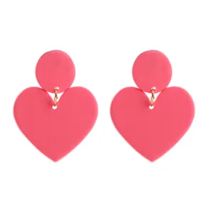 Detaillierte Nahaufnahme süßer rosa herzförmiger Hängeohrringe mit goldenen Ringen für den Alltag.