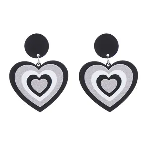Détail en gros plan de boucles d'oreilles cœur en acrylique noir et blanc avec design scintillant.