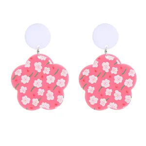 Gros plan détaillé de boucles d'oreilles en acrylique à motif floral rose et clou blanc.