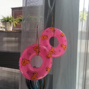 Vue détaillée de boucles d'oreilles bouées roses exagérées avec imprimé de canard jaune.