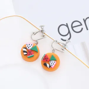 Nahaufnahme handgemachter Fruchtohrringe aus Fimo mit orangen Akzenten und süßen Mini-Anhängern.