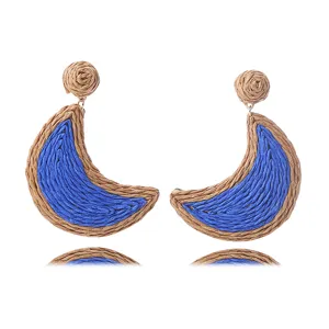Detalle de pendientes de media luna de paja trenzada, elegantes joyas de playa chic.