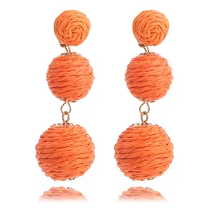 Detailopname van handgemaakte oranje raffia rotan bal lange bungelende oorbellen voor strand.