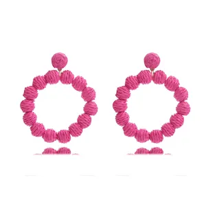 Detailed view of handmade pink raffia woven round statement earrings, bohemian beach style.