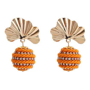 Gros plan détaillé de boucles d'oreilles feuille de ginkgo dorées et sphères strassées.