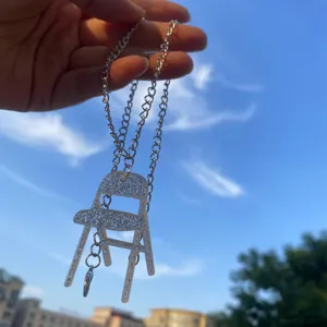 Collier pendentif mini chaise pliante en acrylique pailleté avec détail de chaîne en argent.
