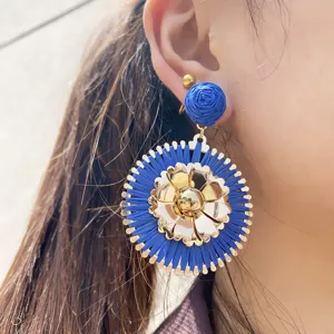 Vue rapprochée d'une boucle d'oreille bohème en raphia bleu avec fleur métallique dorée.