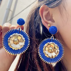 Gros plan détaillé des boucles d'oreilles pendantes en raphia bleu et fleurs dorées.