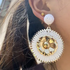 Vue détaillée de boucles d'oreilles pendantes en raphia tissé et fleurs métalliques pour l'été.