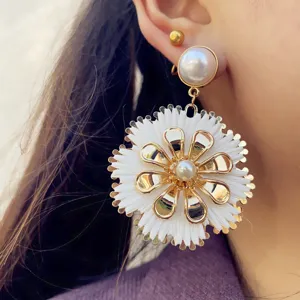 Nahaufnahme von Bohème-Bast-Blumenohrringen mit goldenen Metallelementen und Perle.