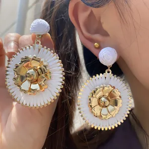 Gros plan détaillé de boucles d'oreilles en raphia tissé avec centre en fleur métal doré.