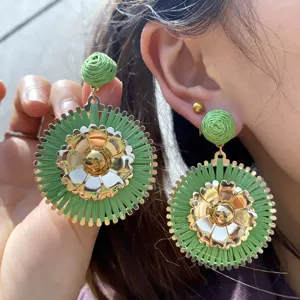 Boucles d'oreilles tendance en raphia vert et fleurs dorées pour un look de vacances élégant.