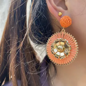Gros plan détaillé de la boucle d'oreille fleur en raphia, mettant en valeur son centre en métal.