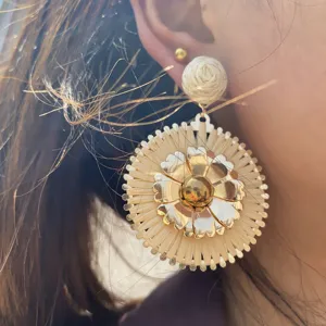 Gros plan de boucles d'oreilles fleuries en raphia tissé fait main, accessoire de vacances.