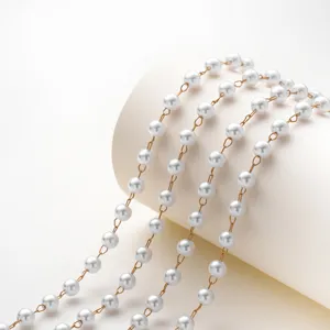Primo piano di una delicata catena di perle bianche collegate da connettori metallici oro.