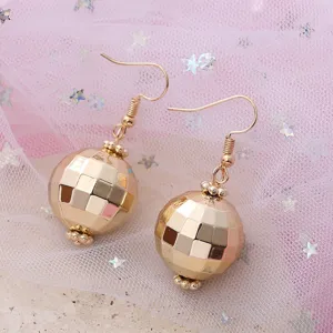 Detailed close-up of retro gold disco ball earrings, minimalist design on pink tulle background.