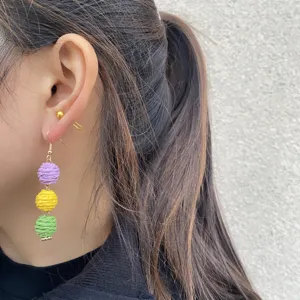 Detailopname van handgemaakte gevlochten oorbellen met paarse, gele en groene ballen.