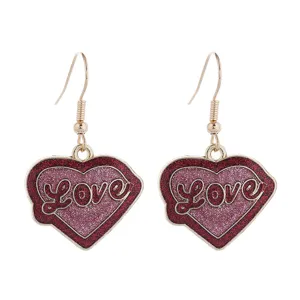 Nahaufnahme von roten Glitzerherz-Ohrhängern mit Love-Schriftzug im eleganten Goldton.