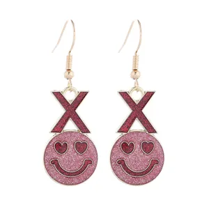 Nahaufnahme rosafarbener Glitzer Smiley Ohrringe mit rotem X Buchstaben und Herzaugen.