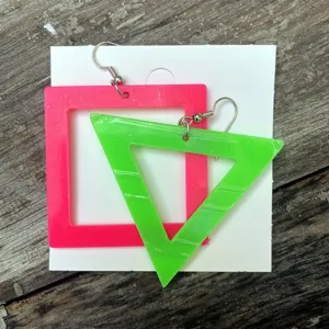 Neon acryl geometrische oirringen detail met levendig roze vierkant en groene driehoek.
