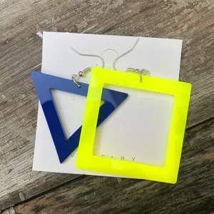 Detailoverzicht van asymmetrische neon acryl oorringen met blauwe driehoek en gele vierkant.