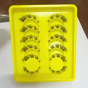 Pestañas postizas agrupadas y esponjosas en bandeja amarilla brillante para maquillaje dramático.