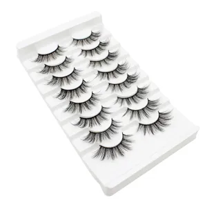 Detaillierte Nahaufnahme von mehreren Paaren dichter künstlicher Wimpern auf einer weißen Schale.