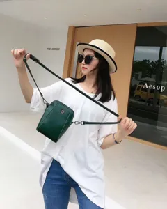 Chic green leather crossbody phone bag with metal flower clasp. Detailed street view shot.